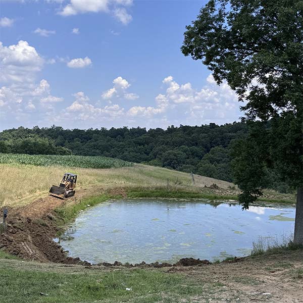 Cleaning and reshaping pond perimeter with a track loader.